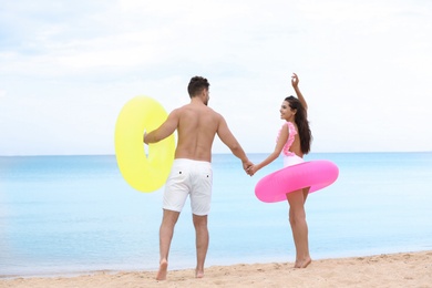 Photo of Happy young couple having fun with inflatable rings on beach near sea