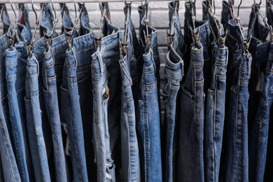 Rack with stylish jeans near brick wall, closeup