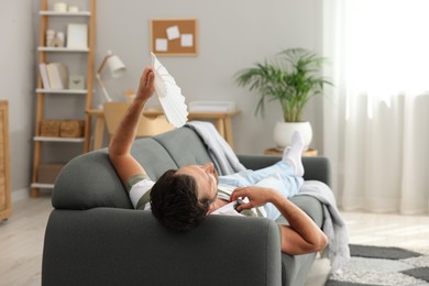 Man waving white hand fan to cool himself on sofa at home