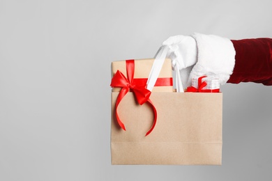 Photo of Santa holding paper bag with gift boxes on light grey background, closeup