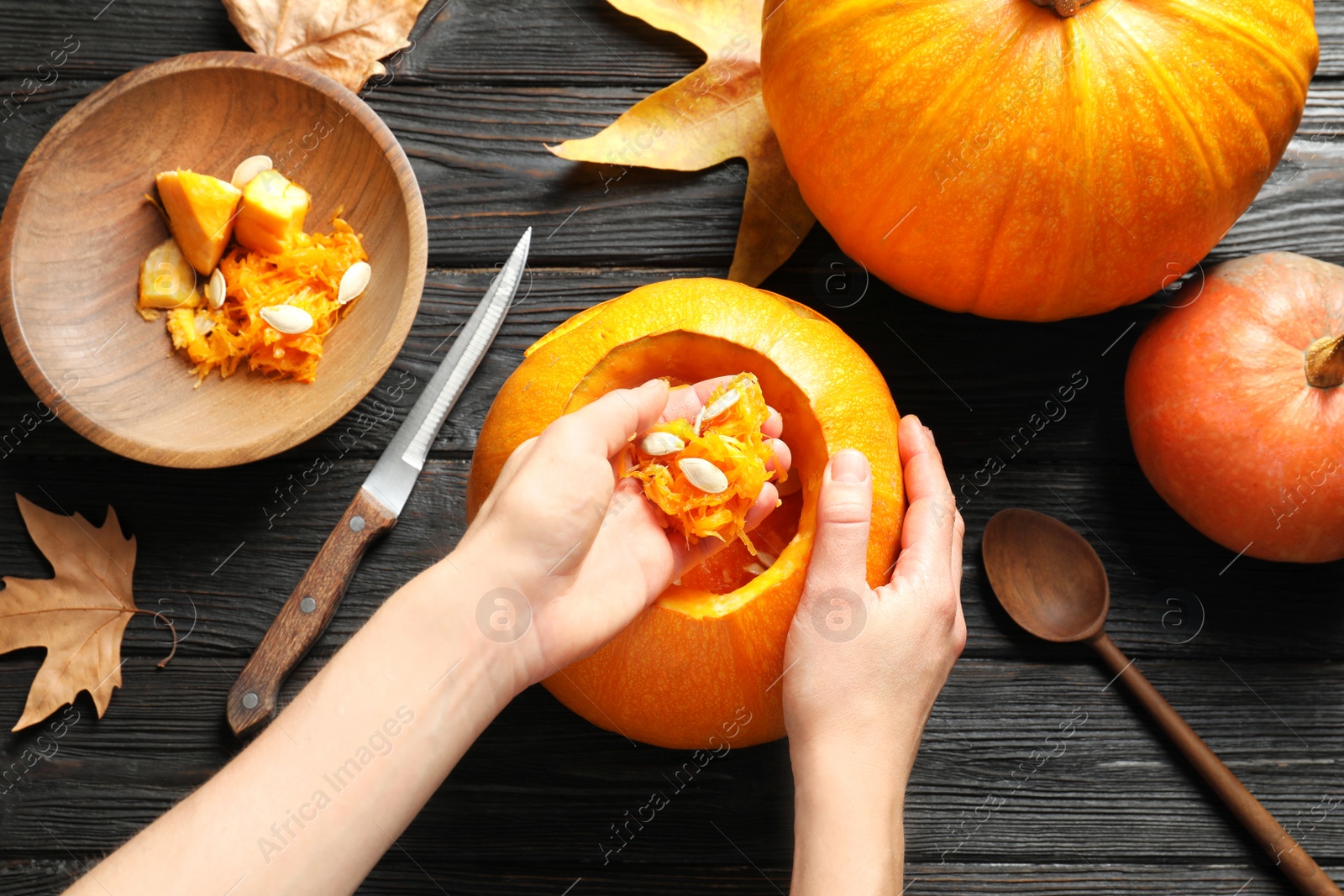 Photo of Woman making Halloween pumpkin head jack lantern on wooden table, closeup