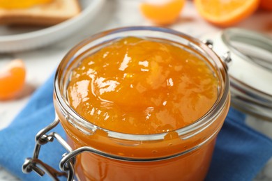 Photo of Tasty tangerine jam in glass jar on table, closeup