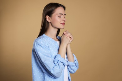 Photo of Woman with clasped hands praying on beige background, space for text