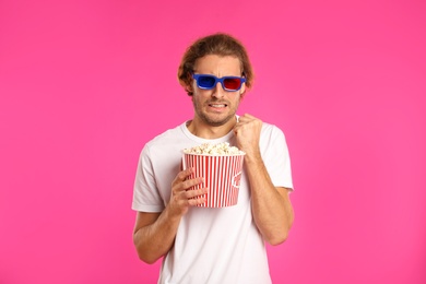 Photo of Emotional man with 3D glasses and popcorn during cinema show on color background