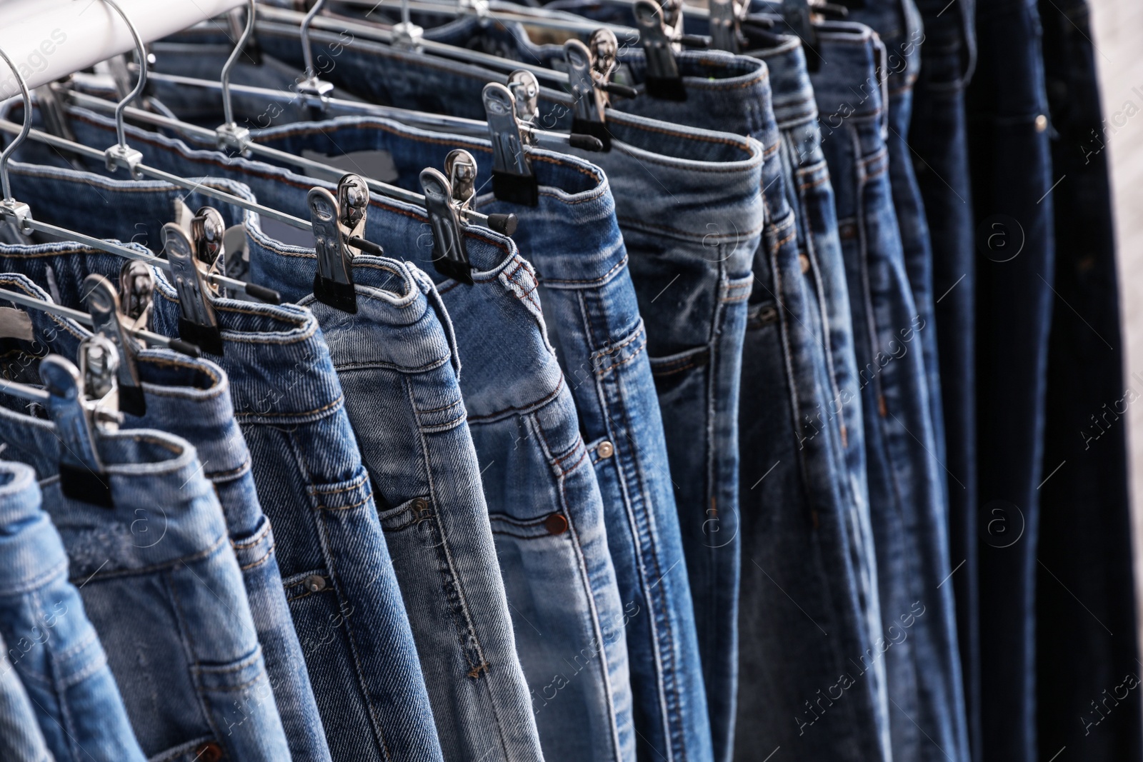 Photo of Hangers with stylish jeans on rack, closeup