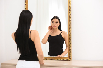 Beautiful young woman looking at herself in mirror indoors