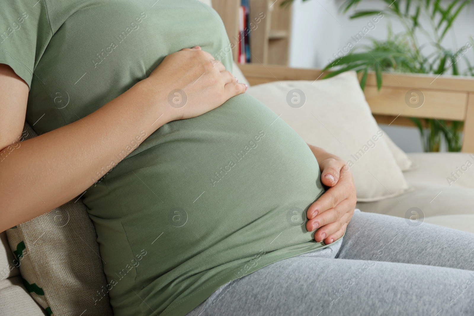 Photo of Pregnant woman touching belly in living room, closeup