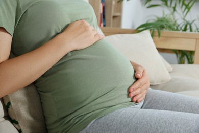 Pregnant woman touching belly in living room, closeup