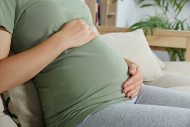 Photo of Pregnant woman touching belly in living room, closeup