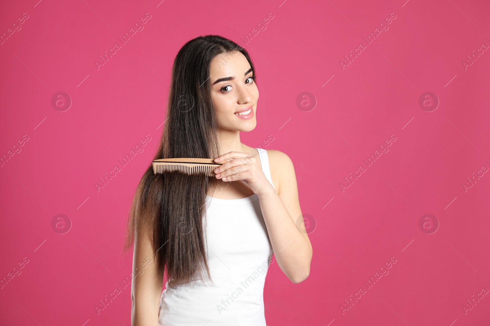 Photo of Beautiful smiling young woman with hair comb on color background