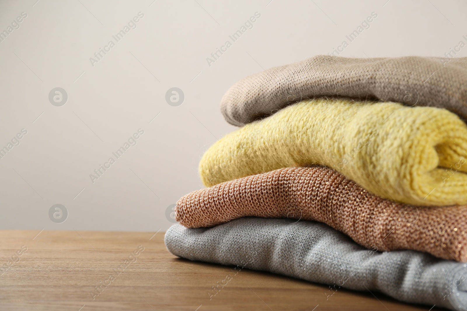 Photo of Stack of knitted sweaters on wooden table, closeup. Space for text