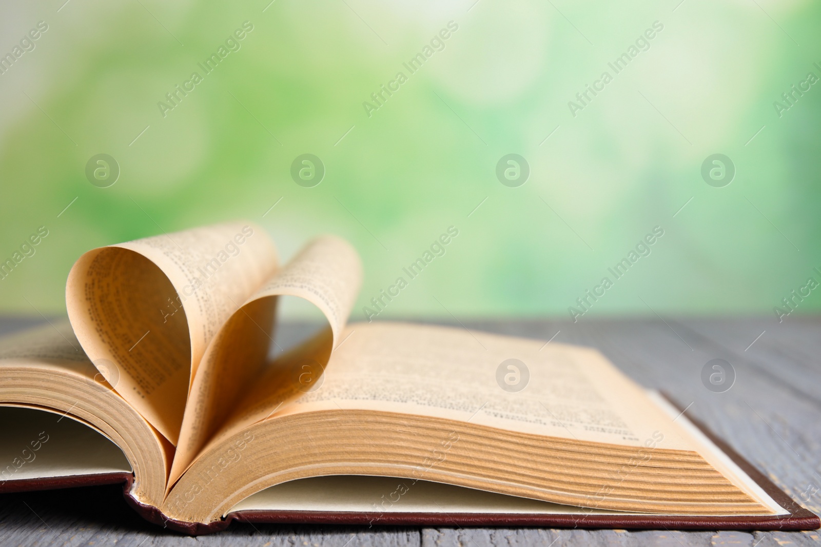 Photo of Open book on grey wooden table against blurred green background, closeup
