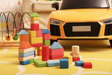 Photo of Colorful building blocks and child's electric car on floor in playroom
