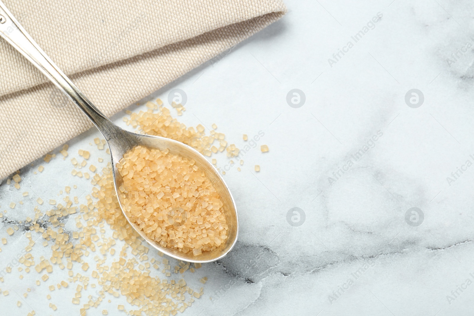 Photo of Spoon with brown sugar on white marble table, top view. Space for text