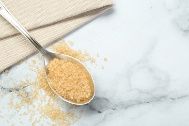 Spoon with brown sugar on white marble table, top view. Space for text