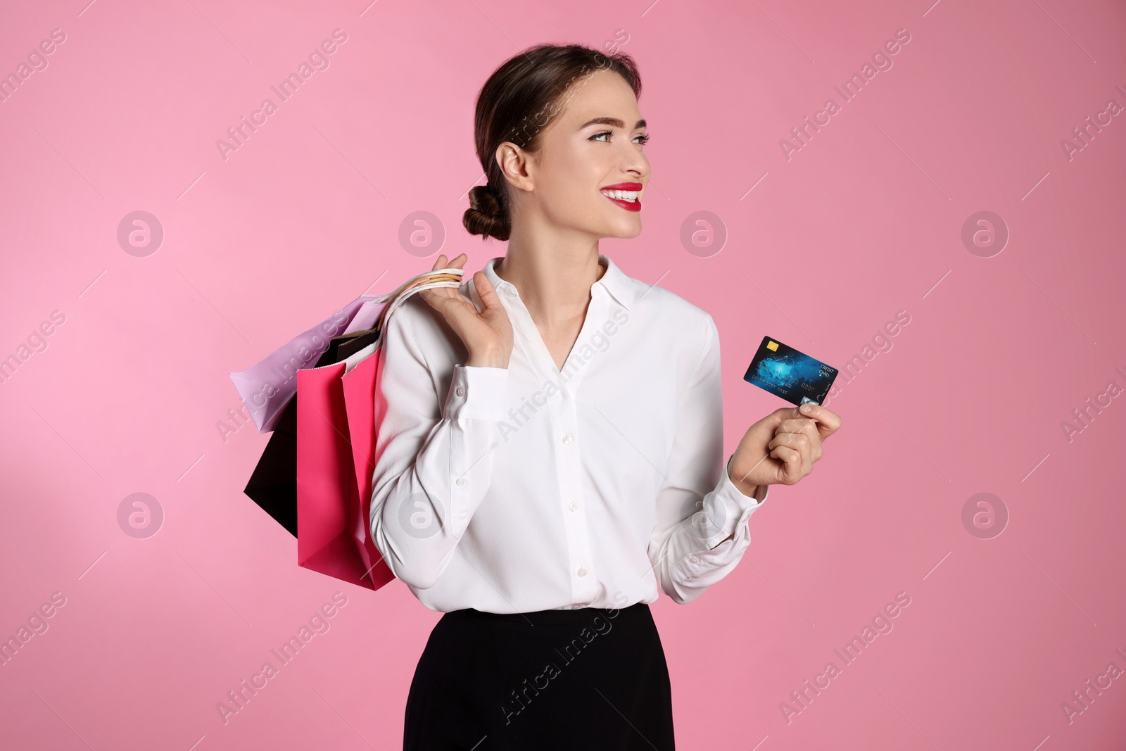 Photo of Happy young woman with shopping bags and credit card on light pink background. Big sale