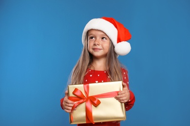 Happy little child in Santa hat with gift box on blue background. Christmas celebration