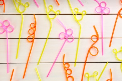 Colorful plastic drinking straws on white wooden table, flat lay
