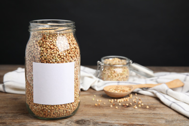 Photo of Organic green buckwheat in jar with blank label on wooden table