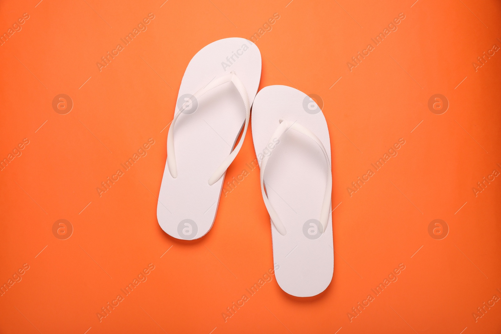 Photo of Stylish white flip flops on orange background, top view