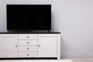 Photo of Modern TV on cabinet near white wall in room. Space for text