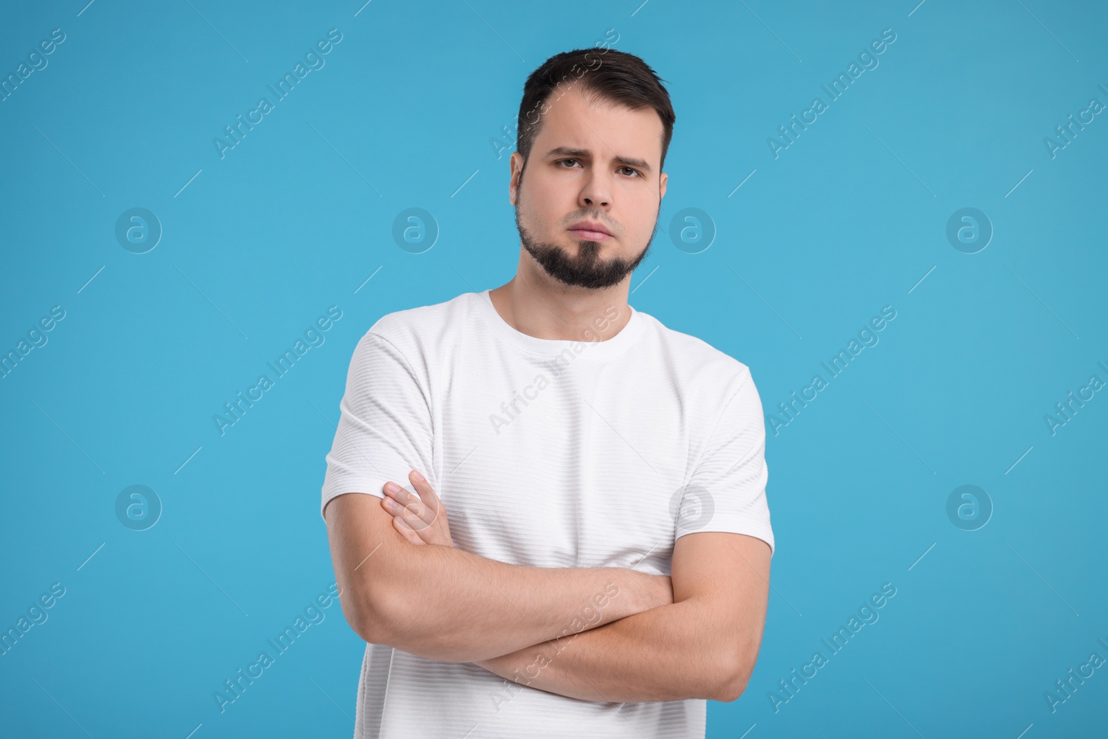 Photo of Portrait of sad man with crossed arms on light blue background