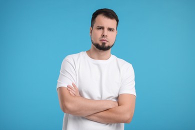 Portrait of sad man with crossed arms on light blue background