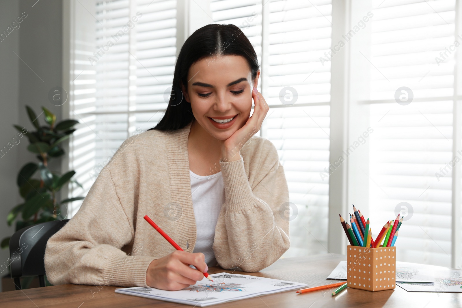Photo of Young woman coloring antistress page at table indoors
