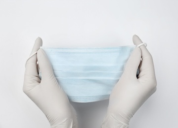 Doctor in medical gloves holding protective mask on white background, closeup