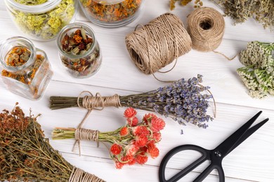 Photo of Bunches of dry flowers, different medicinal herbs, scissors and spools on white wooden table, flat lay