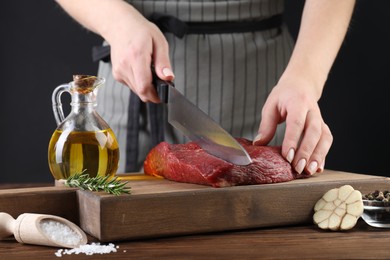 Photo of Woman cutting fresh raw beef steak at wooden table, closeup