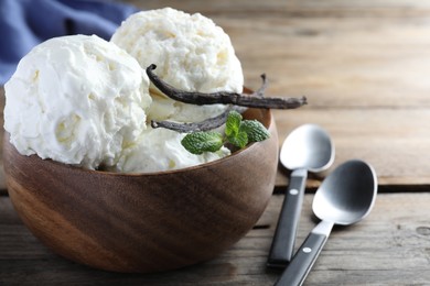 Yummy vanilla ice cream in bowl on wooden table, closeup