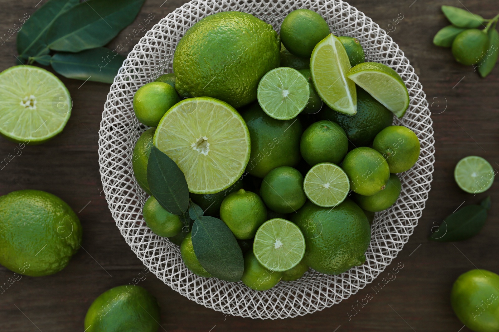 Photo of Fresh ripe limes and green leaves on wooden table, flat lay