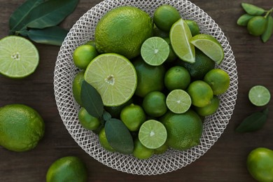 Fresh ripe limes and green leaves on wooden table, flat lay