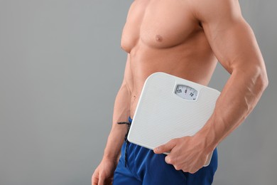 Photo of Athletic man holding scales on grey background, closeup and space for text. Weight loss concept