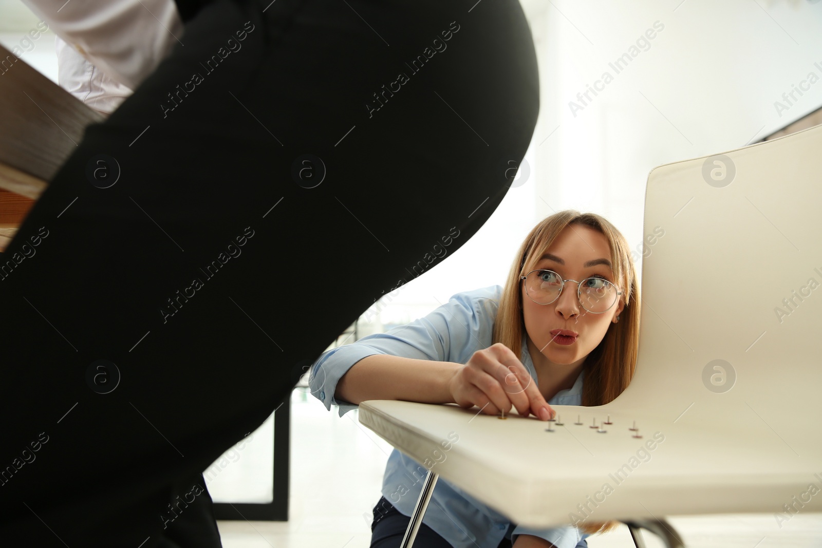 Photo of Young woman putting pins on chair while her colleague sitting down in office, closeup. Funny joke