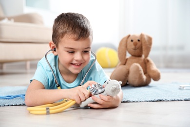 Cute child imagining himself as doctor while playing with stethoscope and toy at home