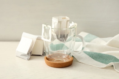 Photo of Drip coffee bags and glass cup on white wooden table