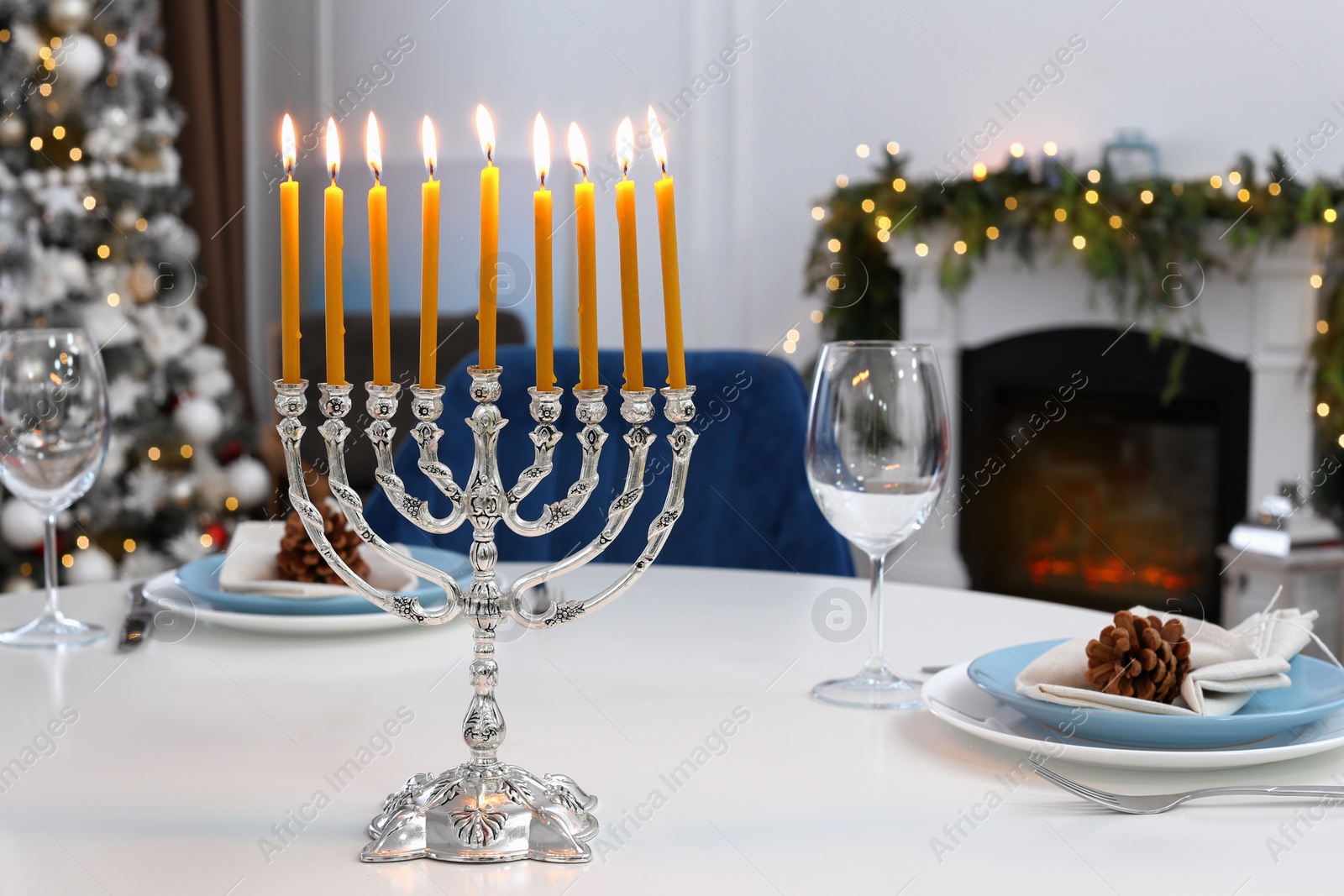 Photo of Silver menorah on white table in room with fireplace and Christmas decorations. Hanukkah symbol