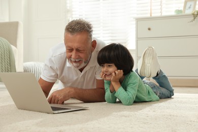 Photo of Happy grandfather and his grandson using laptop together on floor at home