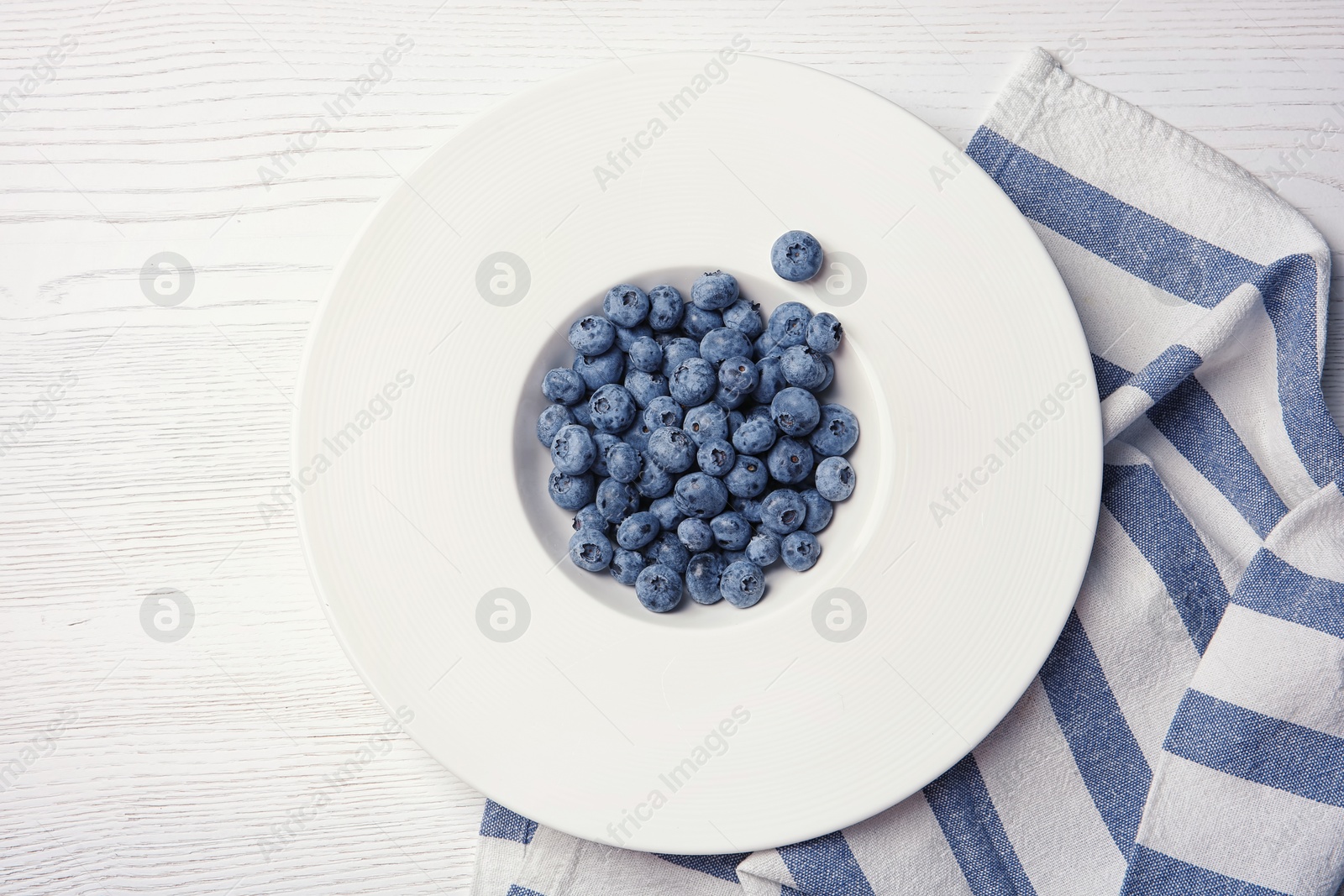 Photo of Fresh blueberries in white plate on wooden background, top view