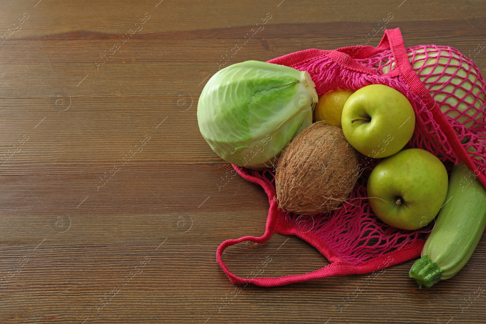 Photo of Net bag with vegetables and fruits on wooden table. Space for text