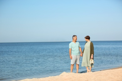 Happy mature couple walking at beach on sunny day