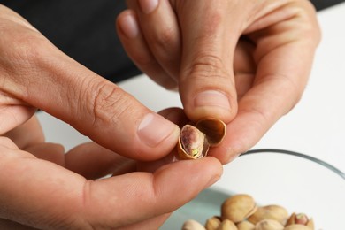Photo of Woman opening tasty roasted pistachio nut at white table, closeup