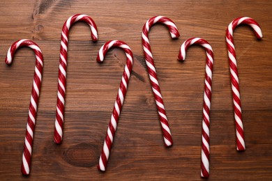 Photo of Sweet Christmas candy canes on wooden table, flat lay