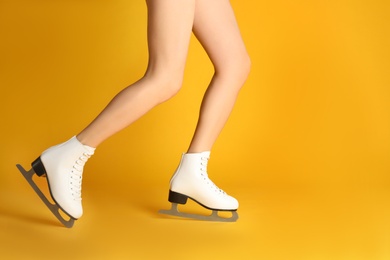 Woman in elegant white ice skates on yellow background, closeup of legs. Space for text