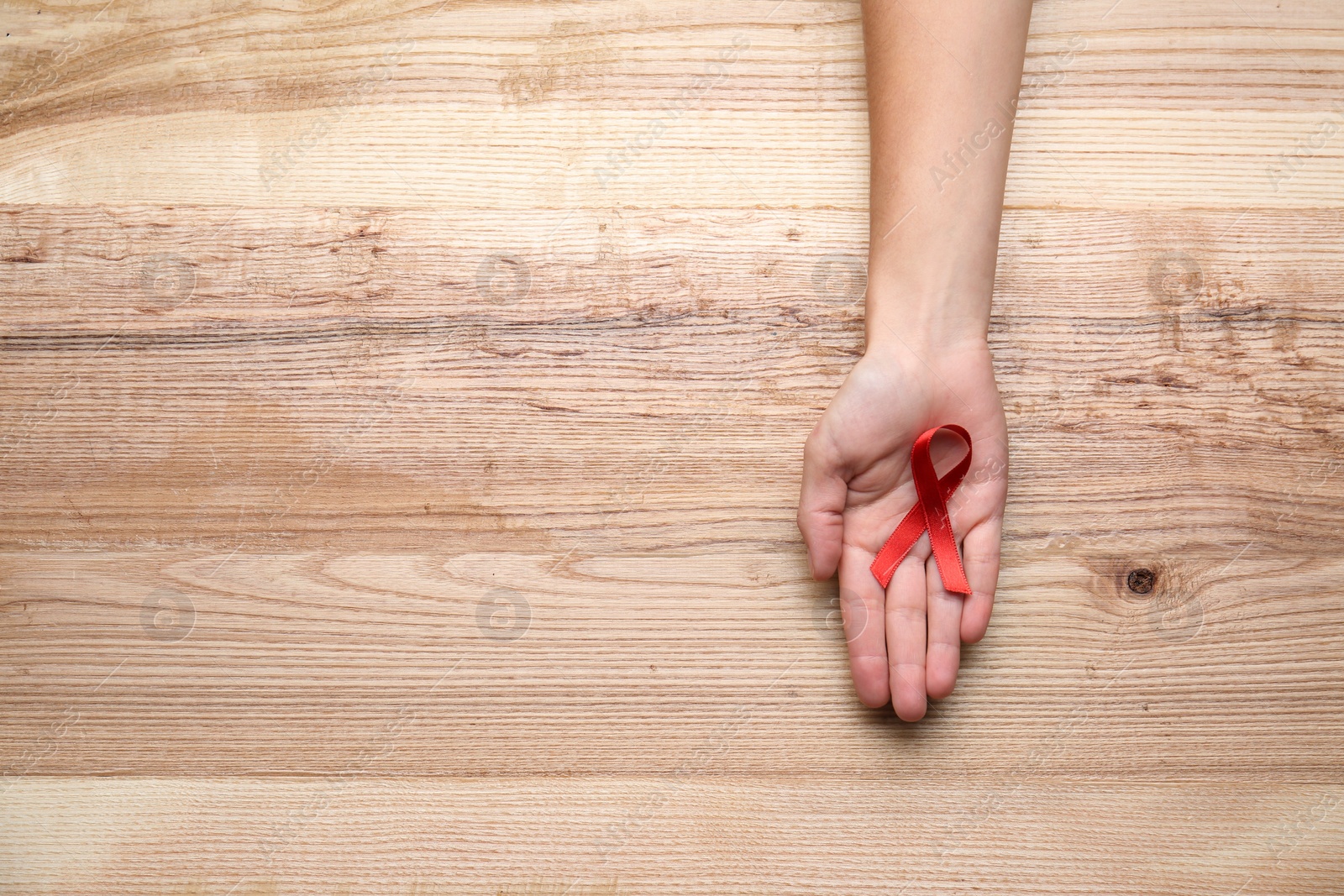 Photo of Woman holding red awareness ribbon on wooden background, top view with space for text. World AIDS disease day