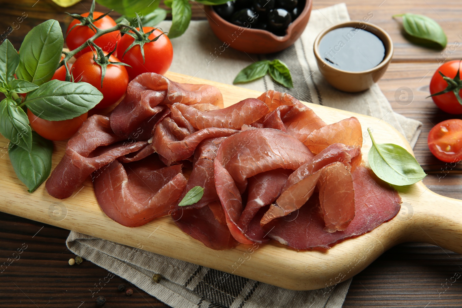 Photo of Board with delicious bresaola served with other snacks on wooden table, closeup