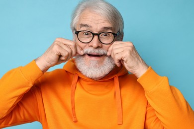 Photo of Senior man touching mustache on light blue background
