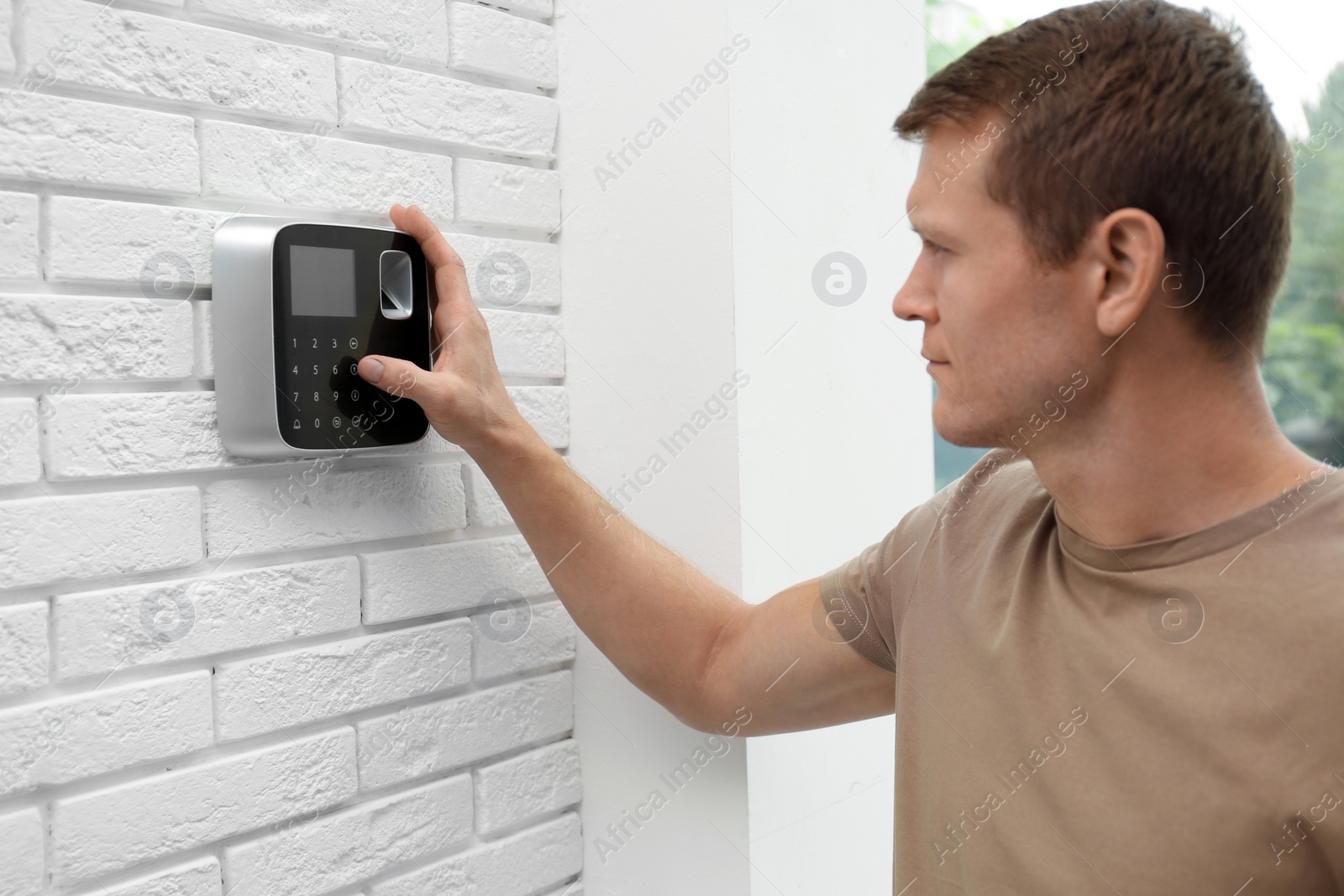 Photo of Handsome man using security alarm system indoors